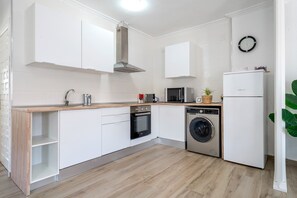 A modern kitchen with white cabinetry, a stainless steel range hood, a microwave, an oven, a washing machine, and a refrigerator. - Holiday Home "Palmera" with Shared Pool & Wi-Fi (Miami-Platja)
