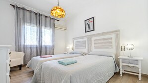Een slaapkamer met twee bedden, een witte ladekast, een nachtkastje met een lamp, en een hanglamp.