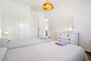 A bedroom with two beds, a white dresser, a mirror, and a door leading to another room.