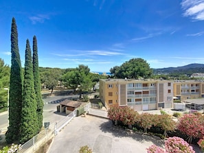 A multi-story building with balconies, a parking area, and surrounding greenery.