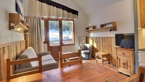 Una habitación acogedora con una mesa de madera, sillas, un televisor y un ventanal con cortinas.