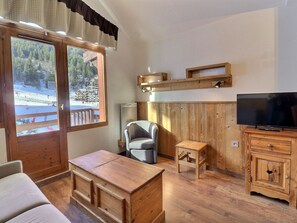Une pièce comprenant un meuble en bois, un téléviseur, une chaise, une petite table et une fenêtre donnant sur un paysage enneigé.