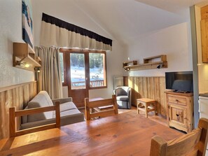 A cozy room with a wooden table, chairs, a television, and a window with curtains.