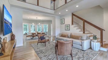 A spacious living area with a high ceiling, a staircase, and a dining area with natural light.