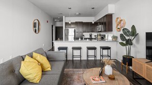 A modern kitchen with dark wood cabinets, a stainless steel refrigerator, and a central island with bar stools. - CozySuites at Notch (Indianapolis)