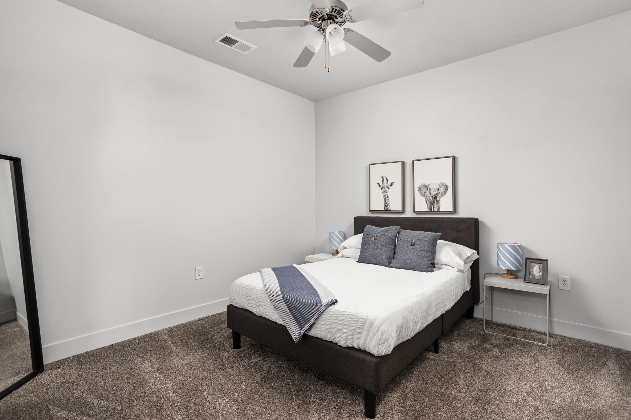 A bedroom with a bed, a nightstand, a ceiling fan, and two framed pictures on the wall.