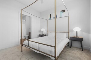 Una cama con dosel y estructura dorada, ropa de cama blanca y dos mesitas de noche con lámparas.