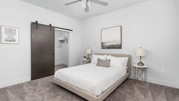 Un dormitorio con cama, ventilador de techo, puerta corredera y dos mesitas de noche con lámparas.