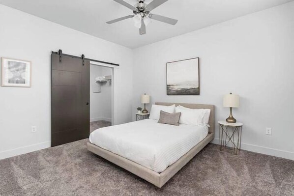 A bedroom with a bed, a ceiling fan, a sliding door, and two bedside tables with lamps.
