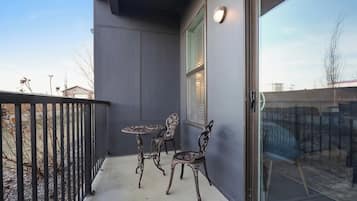 Un balcon avec une balustrade en métal, une porte vitrée et deux tables accompagnées de chaises.