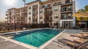 A modern hotel with a swimming pool, outdoor seating, and a multi-story building with balconies. - CozySuites at Notch (Indianapolis)