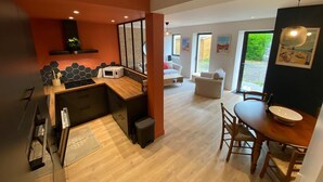 Een moderne keuken met een houten aanrecht, een magnetron en een spoelbak. Er is een zithoek met een tafel en stoelen, en een woonkamer met een bank en een salontafel.