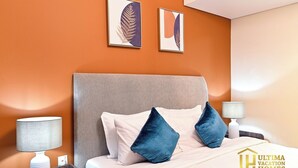 Habitación de hotel con cama, dos almohadas, cabecero, dos lámparas fijadas a la pared y dos obras de arte enmarcadas.