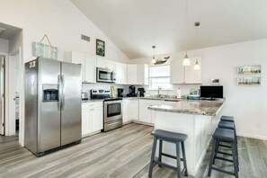 A modern kitchen with white cabinets, stainless steel appliances, a central island with bar stools, and pendant lighting.