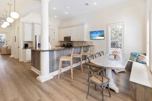 A spacious kitchen with white cabinetry, a central island with seating, and a dining area with a round table and chairs.