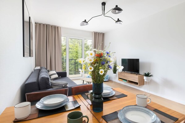 A modern living room with a sofa, dining table, and TV. - Stylish Apartment | Balcony, Close to the Beach (Dziwnów)