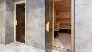 A sauna with a wooden interior and a glass door, set against a grey tiled wall.