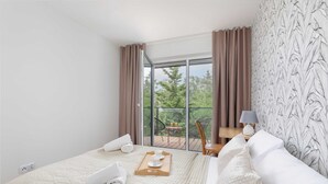 A hotel room with a large bed, a balcony with a table and chairs, and a view of trees.