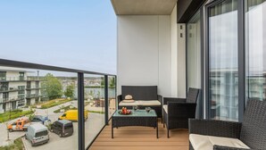 A balcony with wicker furniture, a glass table, and a view of the cityscape.