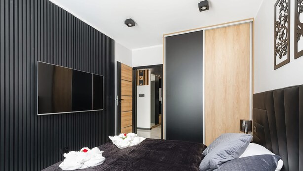 A modern bedroom with a large bed, a flat-screen TV, and a wooden wardrobe.
