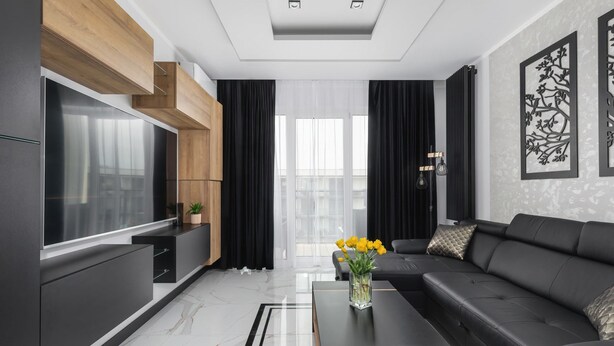 Ein modernes Wohnzimmer mit einem großen Flachbildfernseher, einer schwarzen Ledersofa, einem Couchtisch und einer dekorativen Vase mit Blumen.