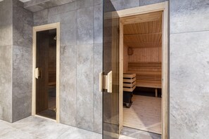 Een sauna met een houten interieur en een glazen deur, voor een grijze betegelde muur.