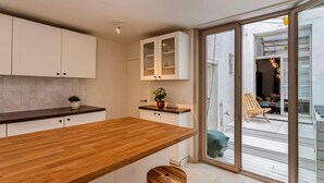 A modern kitchen with a wooden countertop, white cabinets, and a sliding glass door leading to an outdoor seating area. - Spacious house for 6 – central Antwerp (Antwerpen)