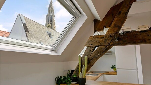 A modern kitchen with a skylight, wooden beams, and a view of a historic tower. - Contemporary 1-BR Duplex in Antwerp (Antwerpen)