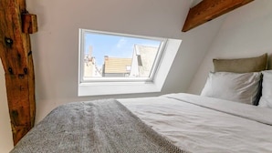 A bedroom with a skylight, a bed, and a view of buildings outside. - Contemporary 1-BR Duplex in Antwerp (Antwerpen)