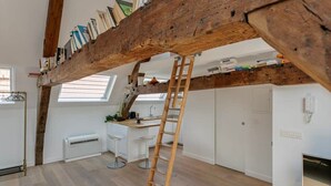 A loft-style room with exposed wooden beams, a ladder, a desk, and a bookshelf. - Contemporary 1-BR Duplex in Antwerp (Antwerpen)