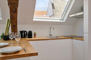 A modern kitchen with a skylight, white cabinets, a wooden countertop, a sink, and a view of a building through the skylight. - Contemporary 1-BR Duplex in Antwerp (Antwerpen)