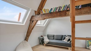 A loft bedroom with a sloped ceiling, a wooden bookshelf, a gray sofa, and a white bean bag. - Contemporary 1-BR Duplex in Antwerp (Antwerpen)