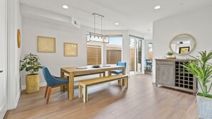 A modern dining area with a wooden table and benches, a hanging light fixture, and a view through a glass door to the outside. - Pacific Beach Paradise by Cardo | Spacious Retreat (San Diego)