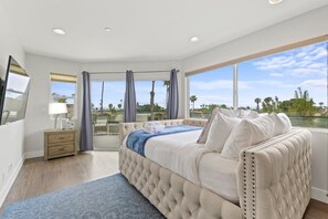 A bedroom with a large bed, a nightstand, a lamp, and a view of the outdoors.