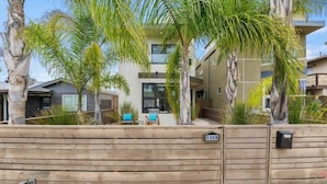 A modern building with a wooden fence, palm trees, and a number '1328' sign. - Pacific Beach Paradise by Cardo | Spacious Retreat (San Diego)