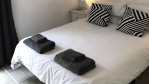 Una cama bien hecha con dos almohadas, una lámpara de noche y un ventilador de techo en una habitación sencilla.