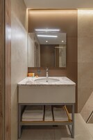 A modern bathroom with a marble sink, wooden paneling, a mirror, and a shelf with folded towels.