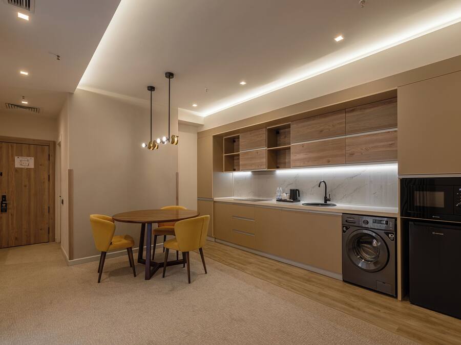 A modern kitchen with a built-in washer and dryer, wooden cabinets, and a dining area with yellow chairs.