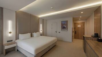 Una habitación de hotel moderna con una cama grande, mesitas de noche, un armario de madera y un escritorio con cafetera.