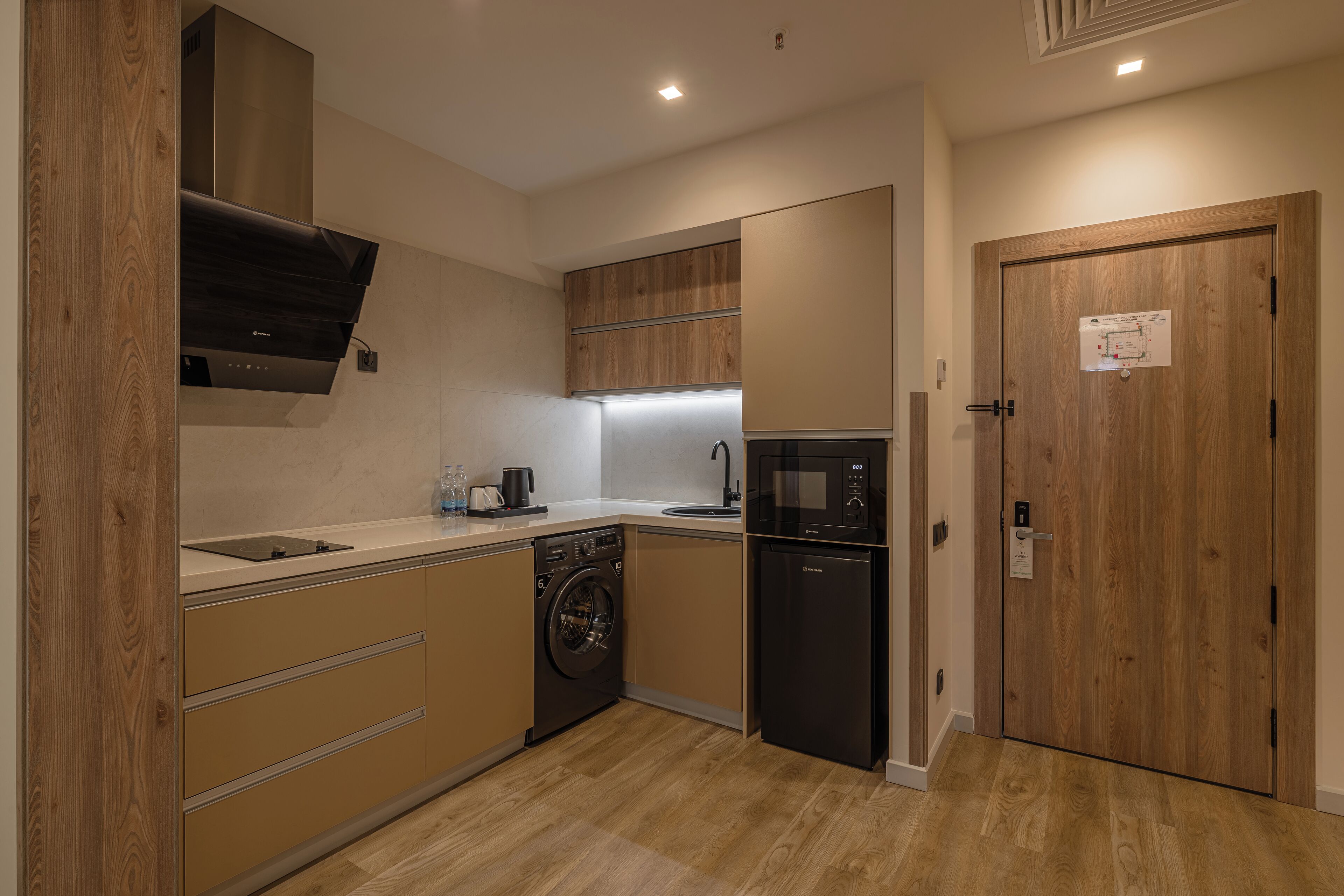 A compact kitchen with wooden cabinets, a built-in washing machine, a microwave, and a sink.