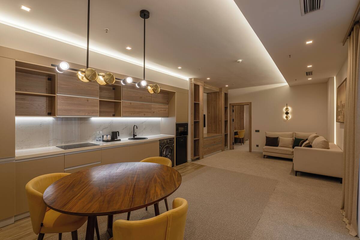 A modern kitchen with wooden cabinets, a dining table with yellow chairs, and a built-in oven.