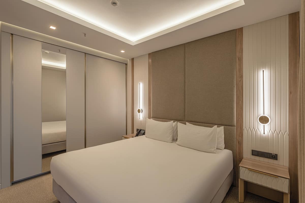 A hotel room with a large bed, a bedside table, a nightstand, a mirror, and a wardrobe.