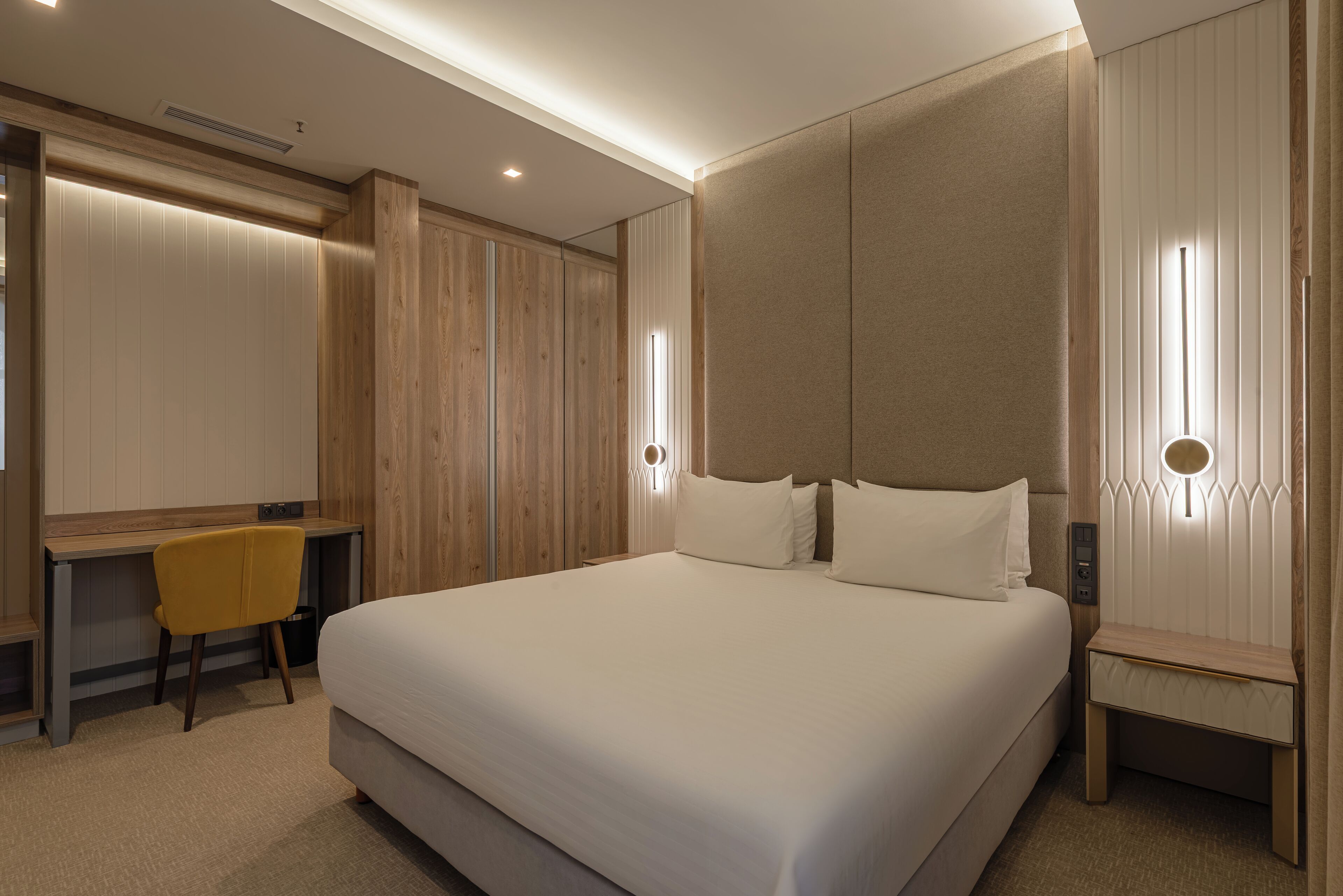 A modern hotel room with a large bed, a desk, and a chair.