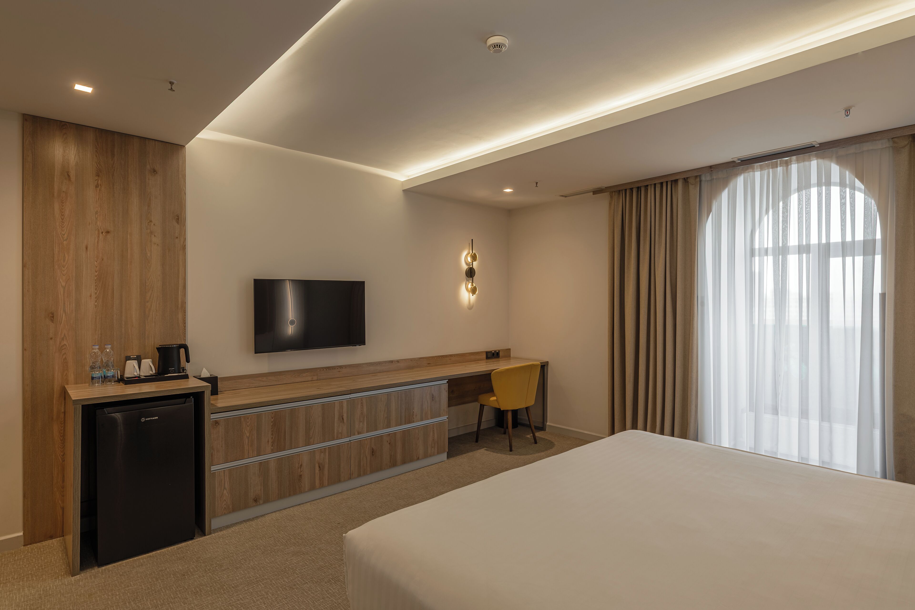 A hotel room with a bed, a desk, a television, and a minibar.