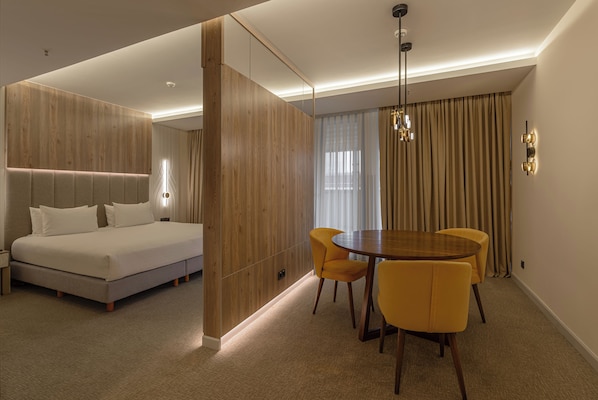 Une chambre d’hôtel moderne avec un lit, une table à manger entourée de chaises jaunes et un mur de séparation en bois.