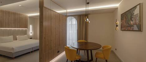 A modern hotel room with a wooden accent wall, a bed, a dining table with four chairs, and a painting on the wall.