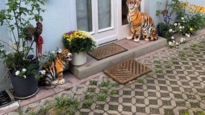 Une maison avec une porte d’entrée, un petit jardin agrémenté de plantes en pot et une statue de tigre.