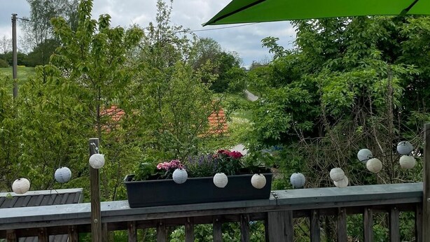 Une terrasse en bois agrémentée d’un parasol vert, de plantes en pot et de sphères décoratives.