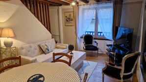 Un saló tranquil i acollidor amb un sofà, cadires, una taula de dinar, un televisor i una escala.