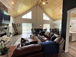 A spacious living room with a high ceiling, a fireplace, a large brown leather sofa, and a dining area with chairs and a table. - The Great Escape Chalet @ Spring Brook Resort (Wisconsin Dells)